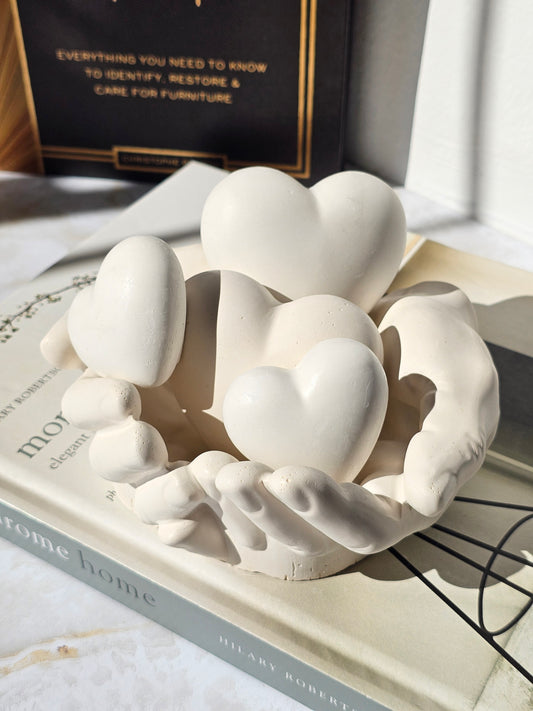 Handcrafted stone-look sculpture of hands gently holding multiple hearts, designed as a meaningful modern decor piece and sentimental gift.